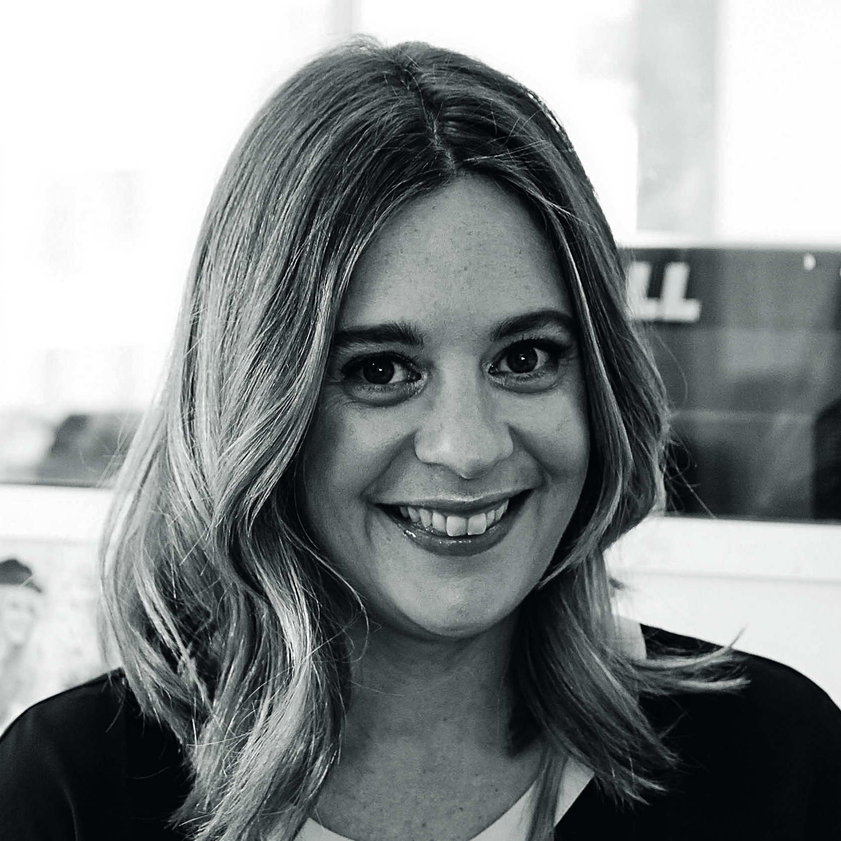 A woman with shoulder-length hair smiling in a black and white photograph, indoors.