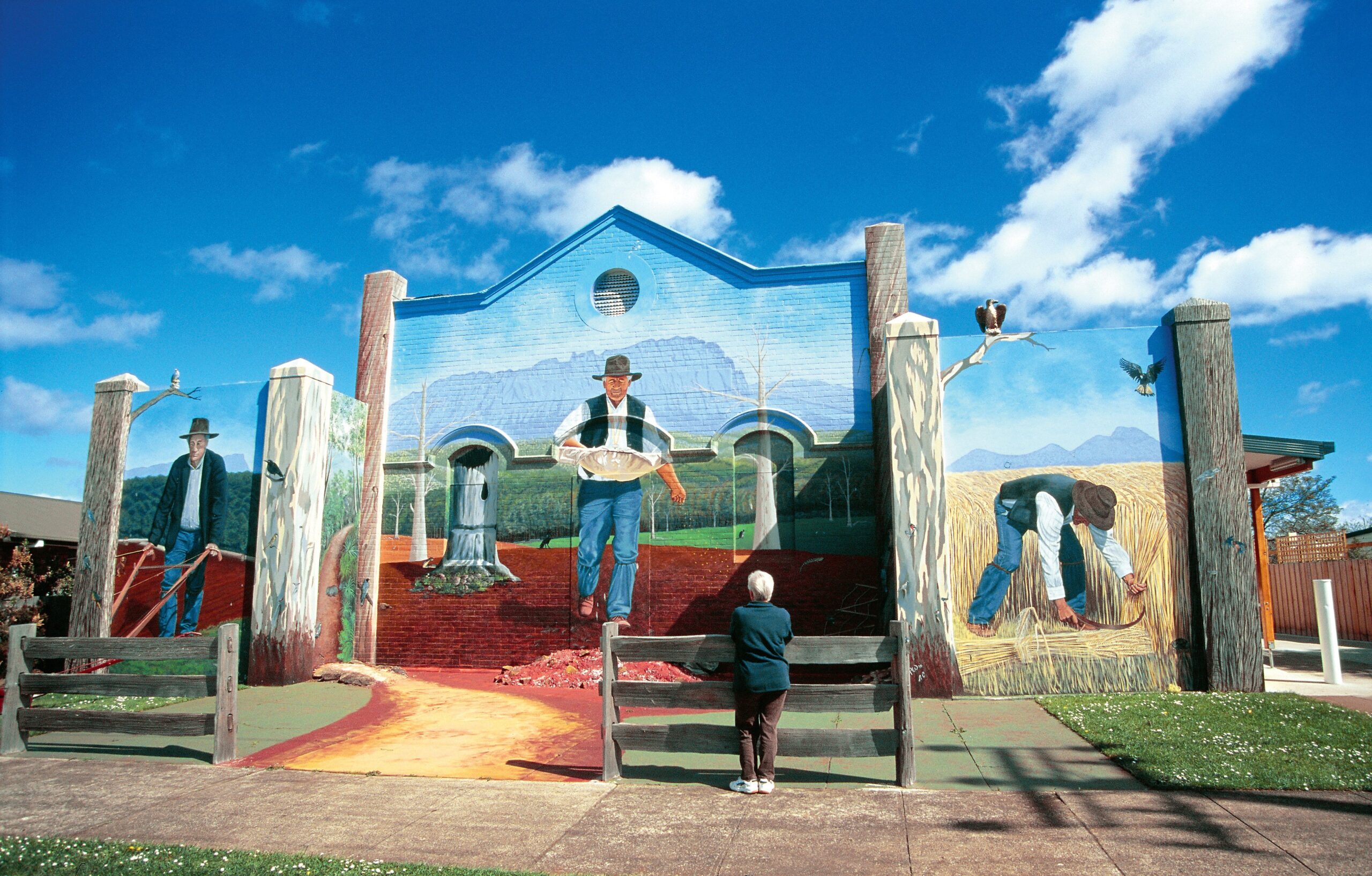 An elderly person stands in front of oversized murals in Sheffield in Tasmania