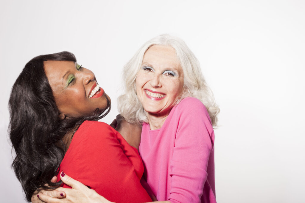 two older ladies with bold makeup hugging and smiling 
