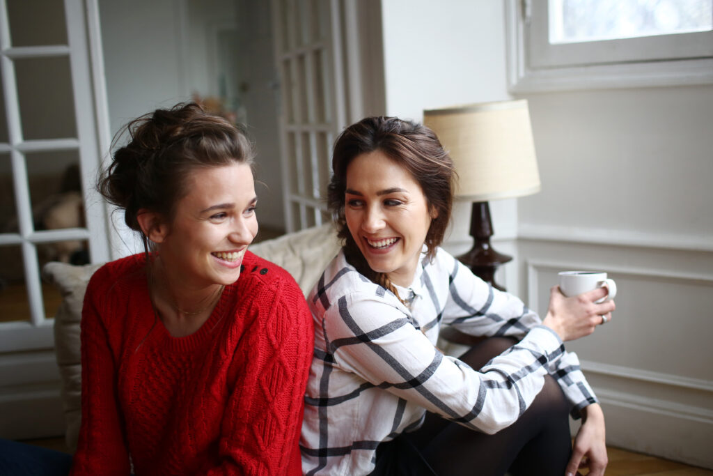 two women smiling at each other,one is drinking coffee.