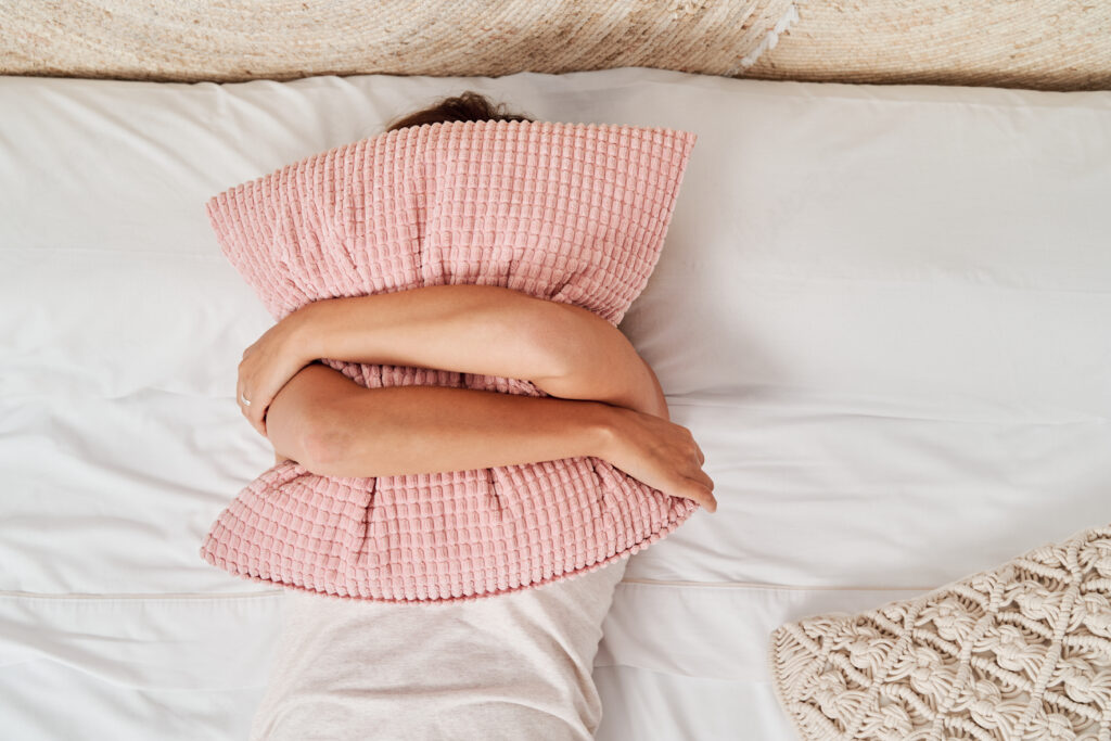 Top view of a beautiful young woman lying in bed covering her face with a pillow to represent sleep need not being met.