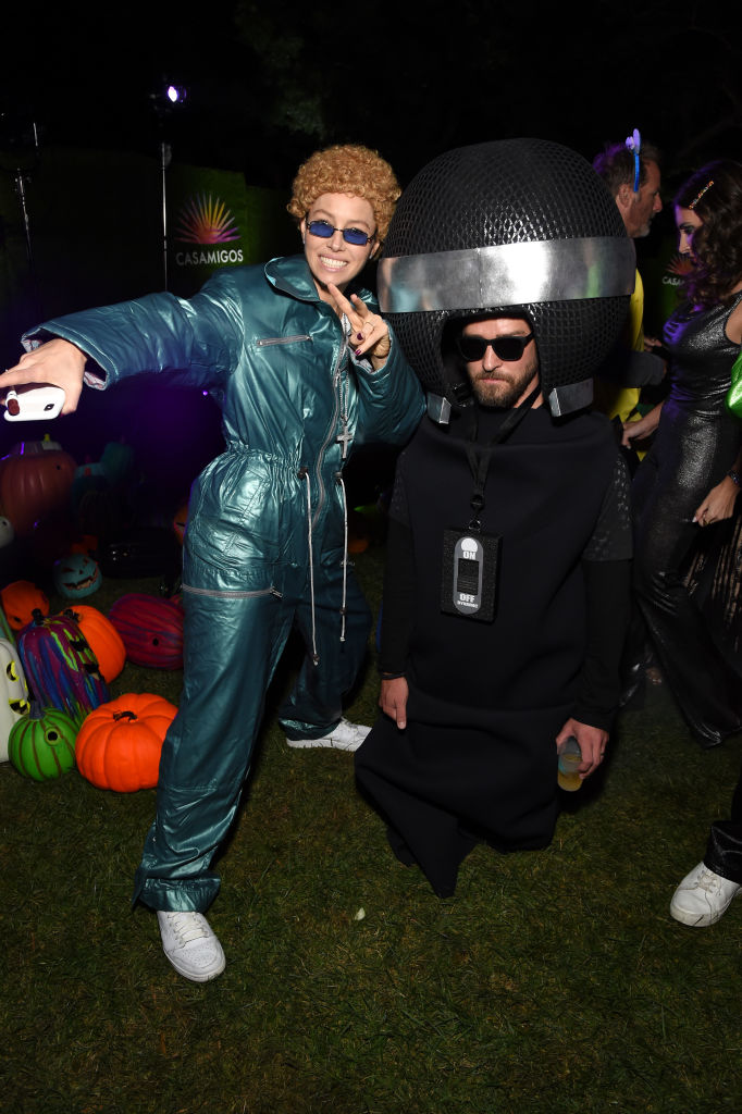 Two people in creative costumes at a Halloween party, one in a blue jumpsuit, the other with a large spherical headpiece.