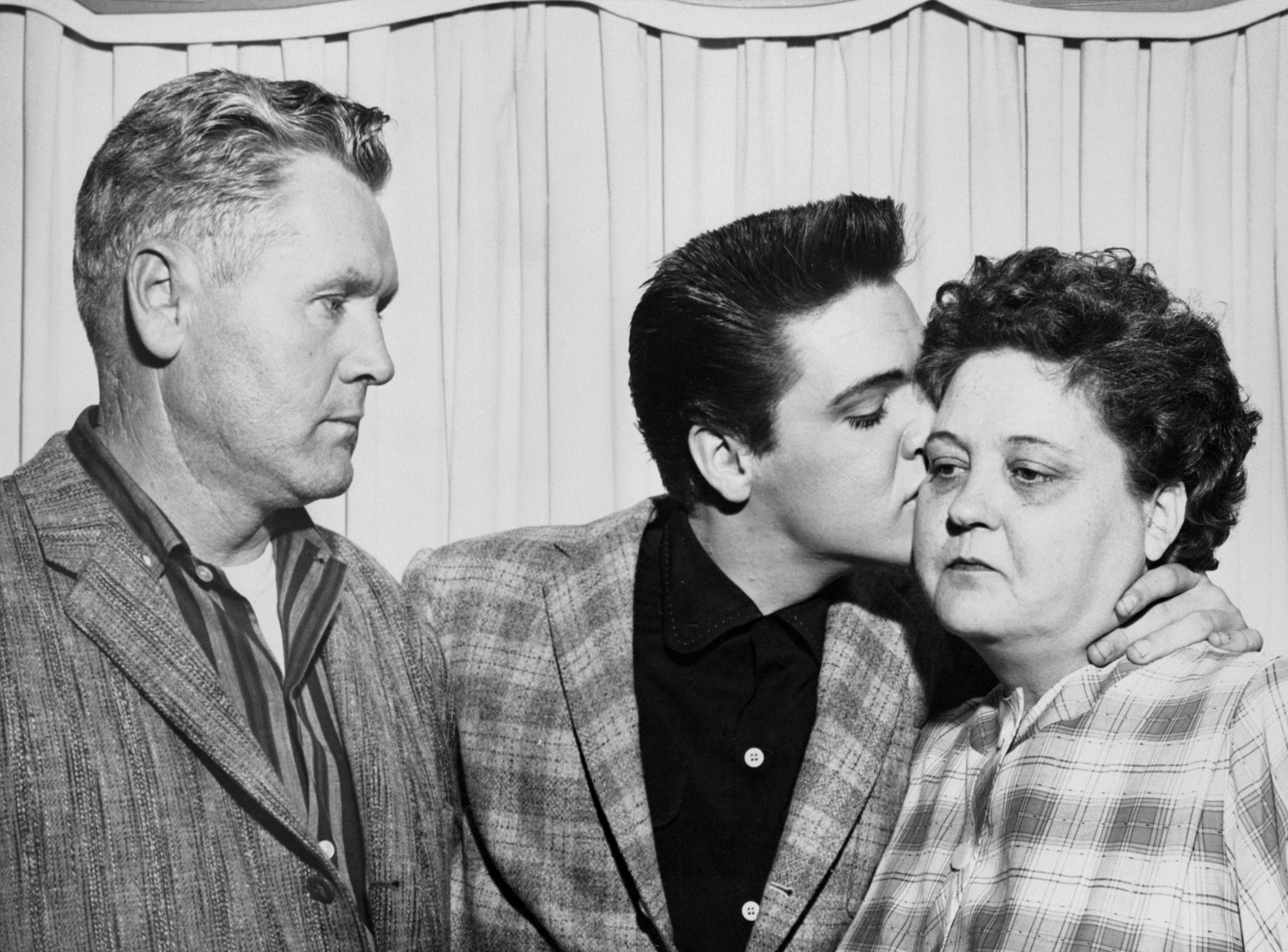 Singer Elvis Presley kisses his mother, Gladys, on the eve of his induction into the Army. At left is his father, Vernon.