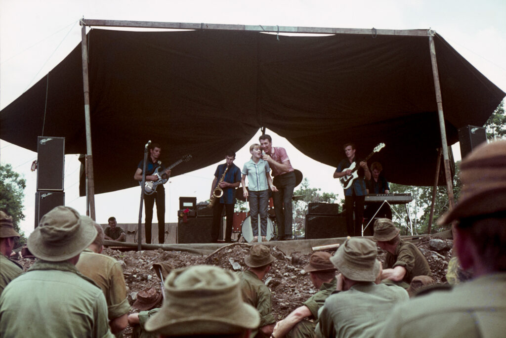 An Australian man and woman with a band of entertainers performing to soldiers in the Vietnam war. 