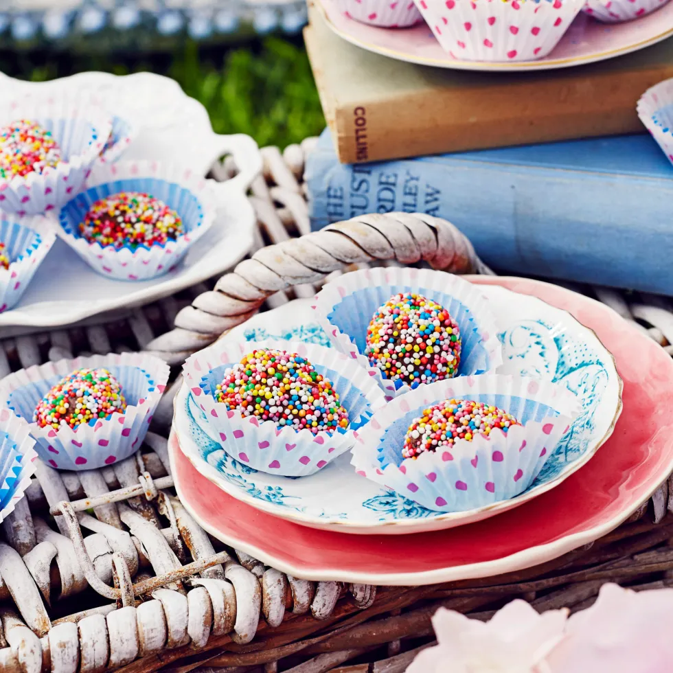 Colorful sprinkle-covered chocolate balls in polka dot paper cups on a woven basket.