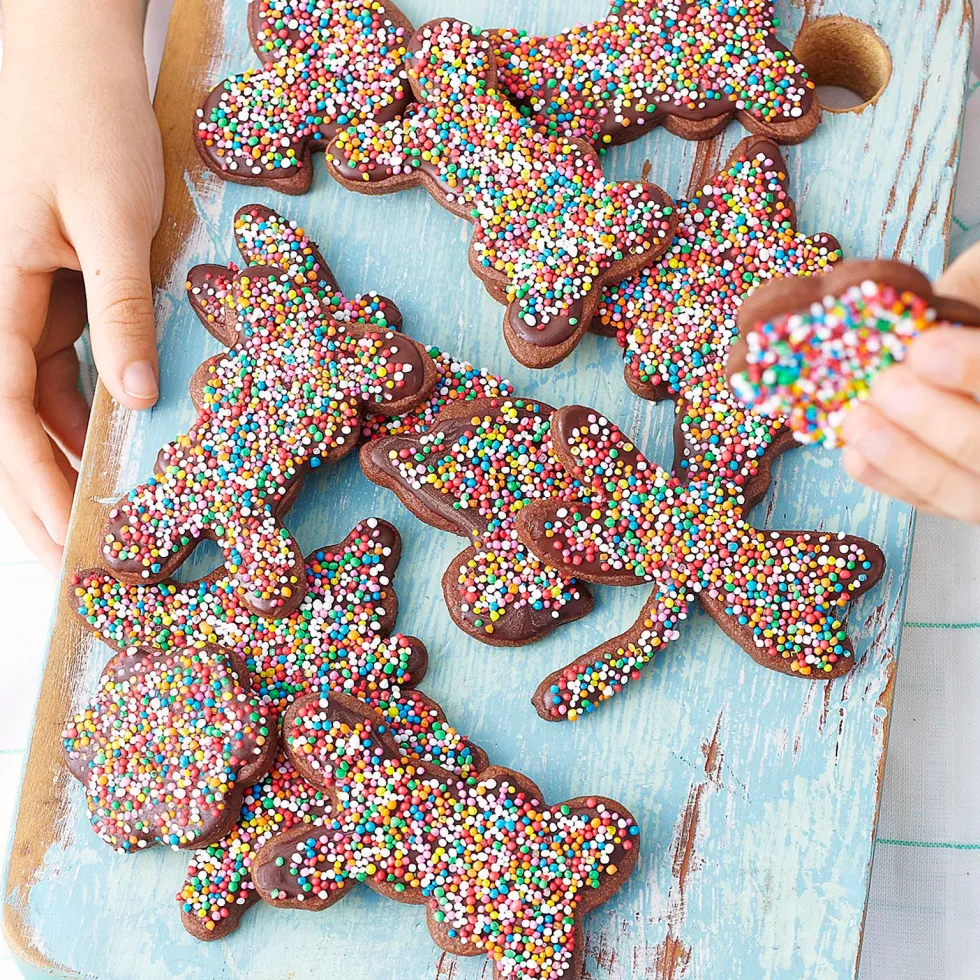 Chocolate cookies shaped like animals, topped with colorful sprinkles, on a blue wooden board.