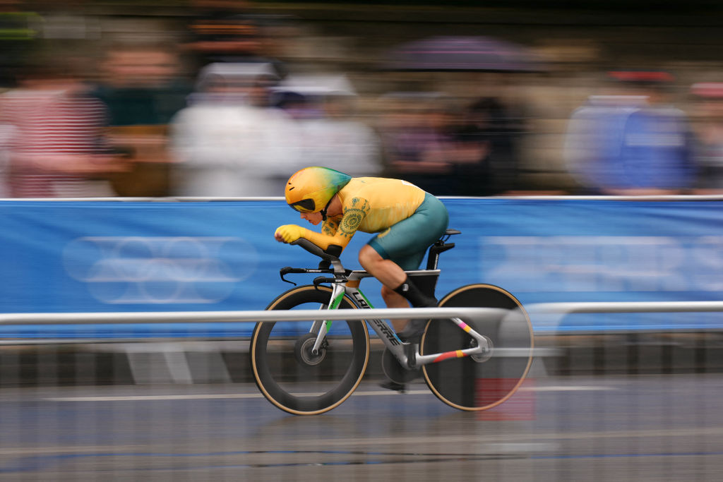 A cyclist wearing a yellow helmet and green suit rides a bike at high speed during a race.