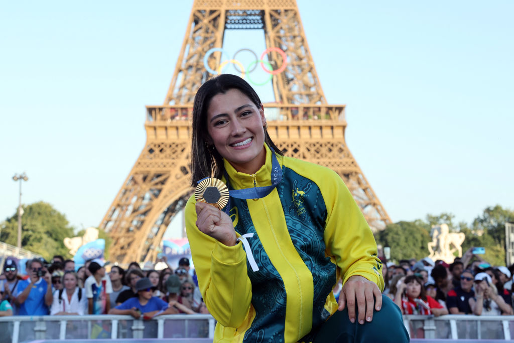 Athlete wearing a yellow jacket holds a medal in front of the Eiffel Tower during an Olympic event.