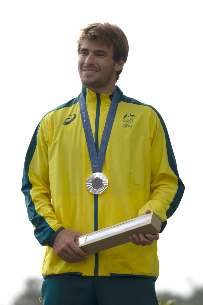 Man in an Australian tracksuit with a silver medal and box at an awards ceremony.