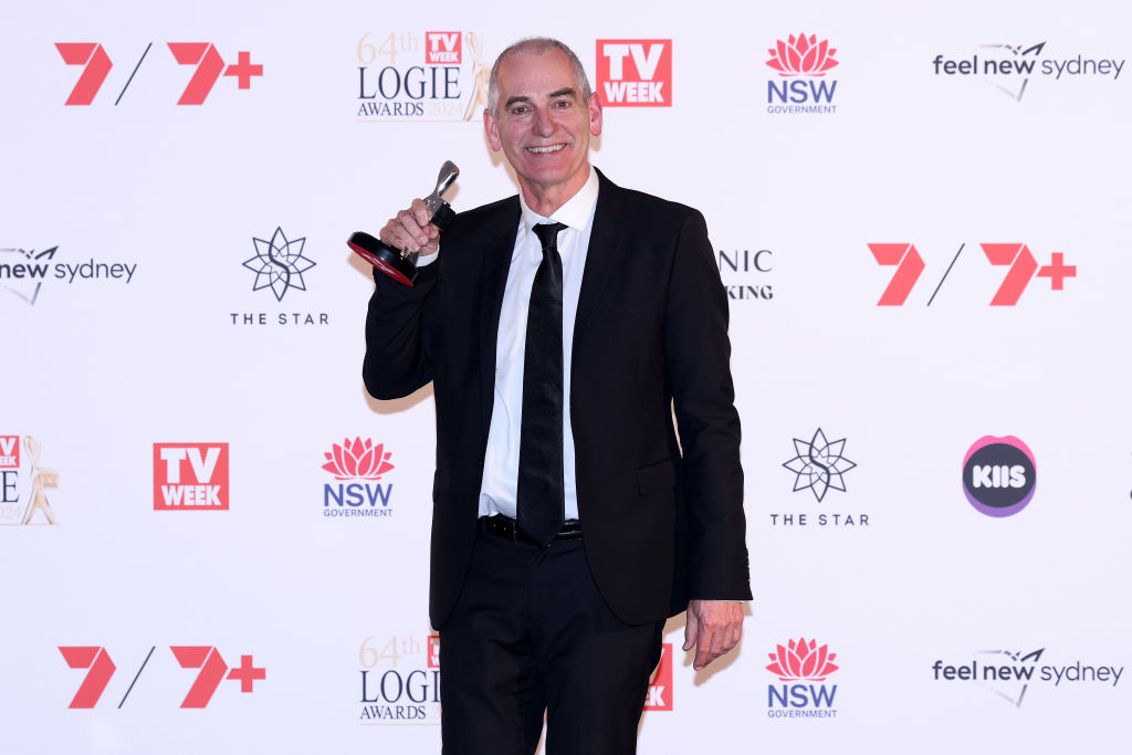 Man in suit holding a Logie award at the 64th TV Week Logie Awards 2023, standing in front of a branded backdrop.