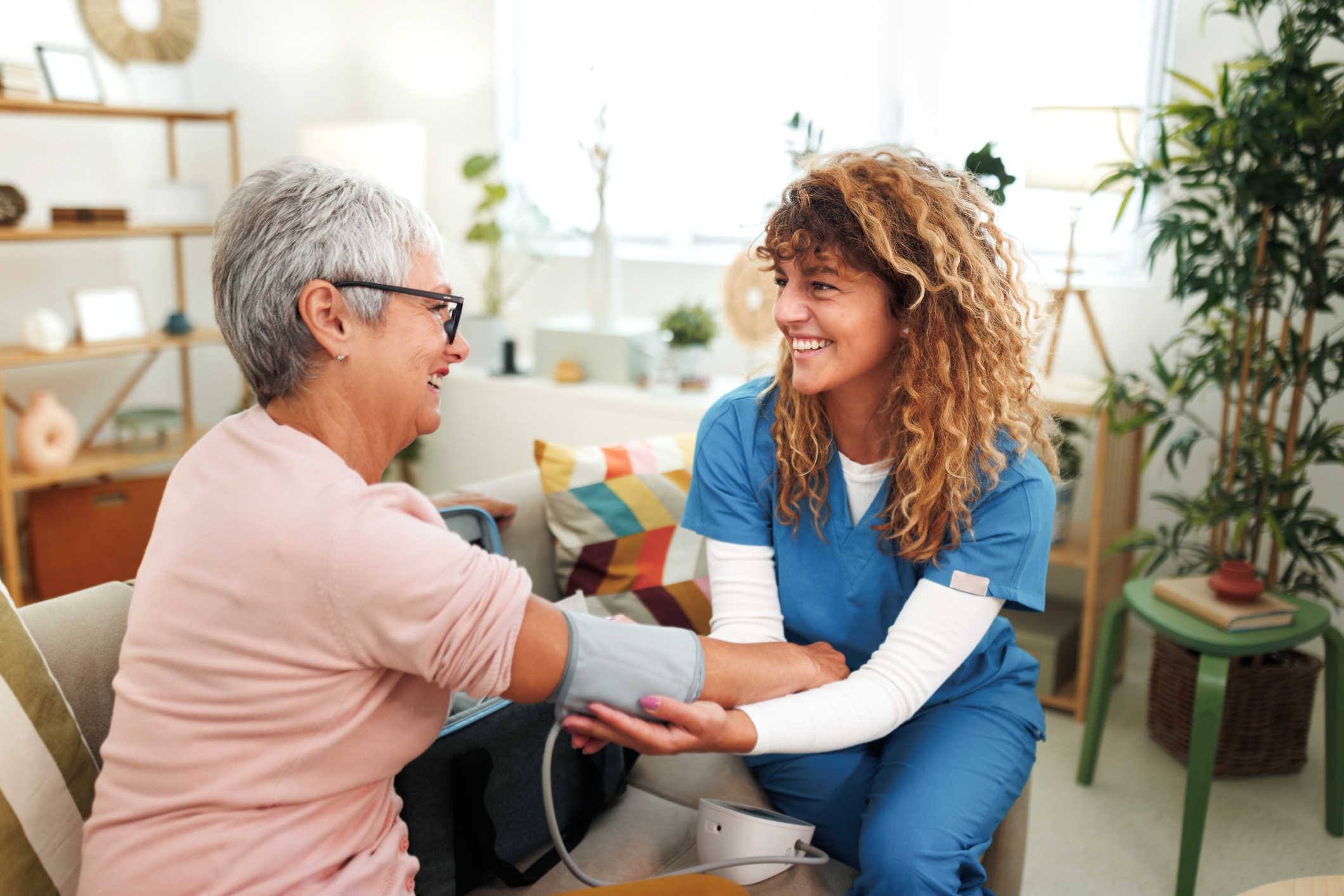 Senior woman having blood pressure checked by home caregiver at apartment