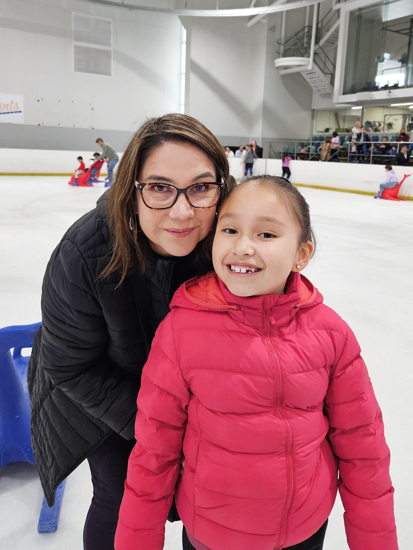 Tairyn in a black puffer coat, and Chloe is a bright pink one, smile for a photo at the ice-skating rink.