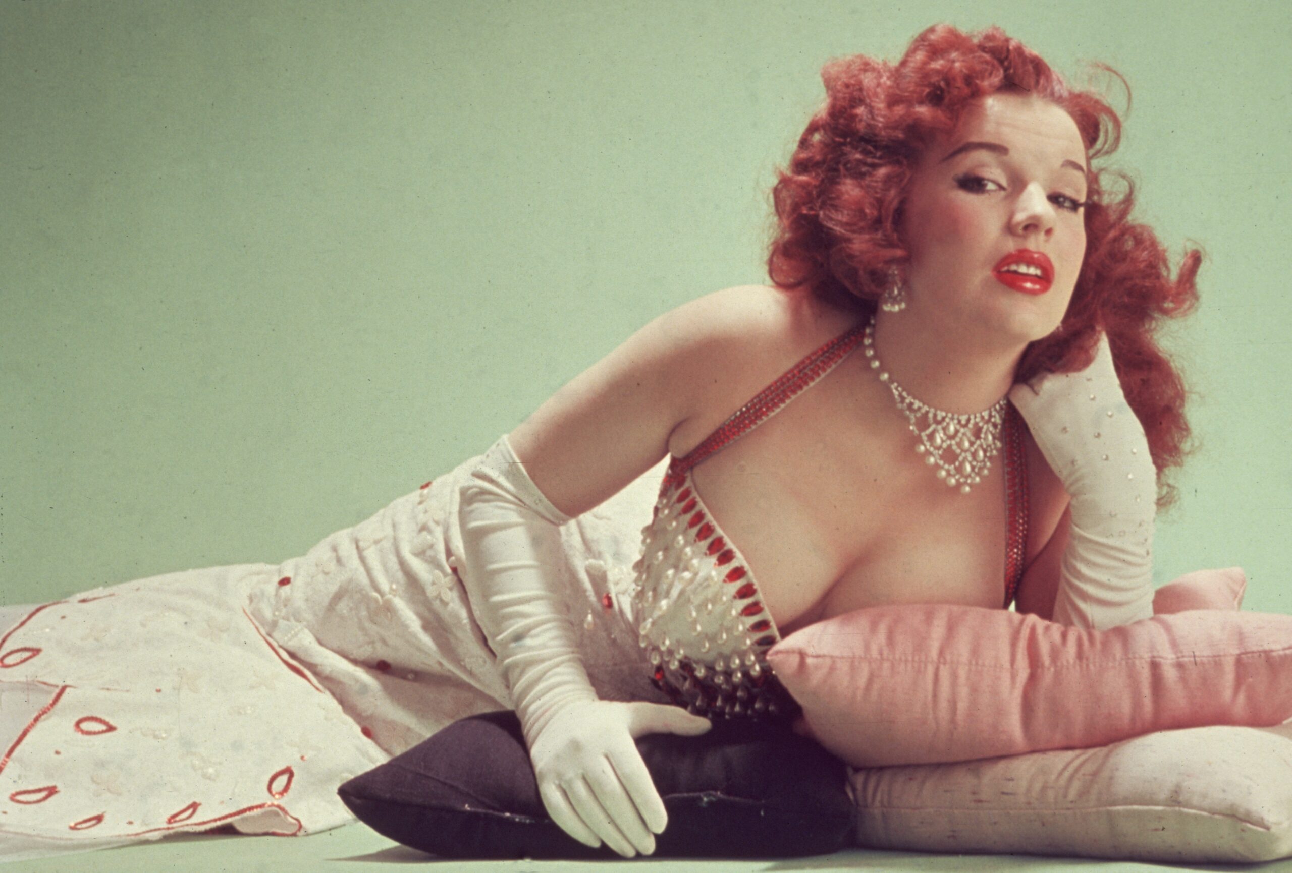 circa 1955:  Studio portrait of Blaze Starr, reclining on pillows on the floor, wearing a red-trimmed white dress and white elbow-length gloves.  (Photo by Hulton Archive/Getty Images)